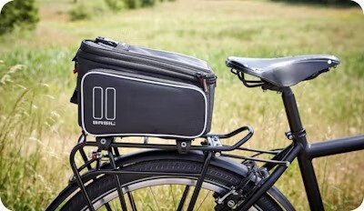 Black bike rack bag securely attached to a bicycle, set against a backdrop of a grassy field.