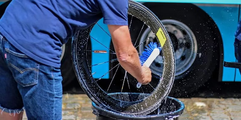 Person cleaning a bicycle wheel with a brush and soapy water.
