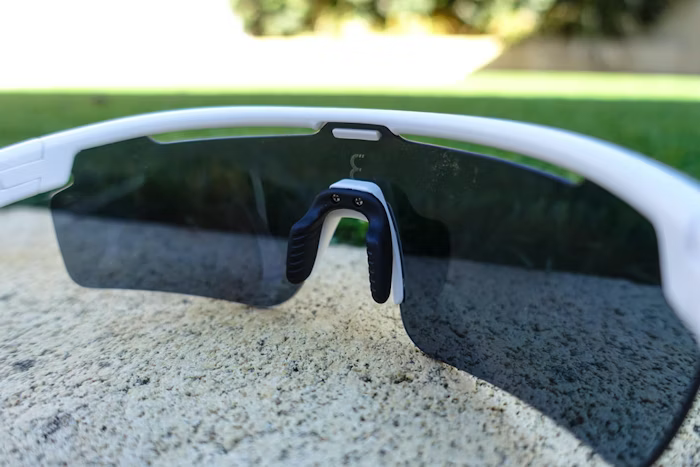 White sports sunglasses with black tinted lenses resting on a concrete surface, grass in the background.