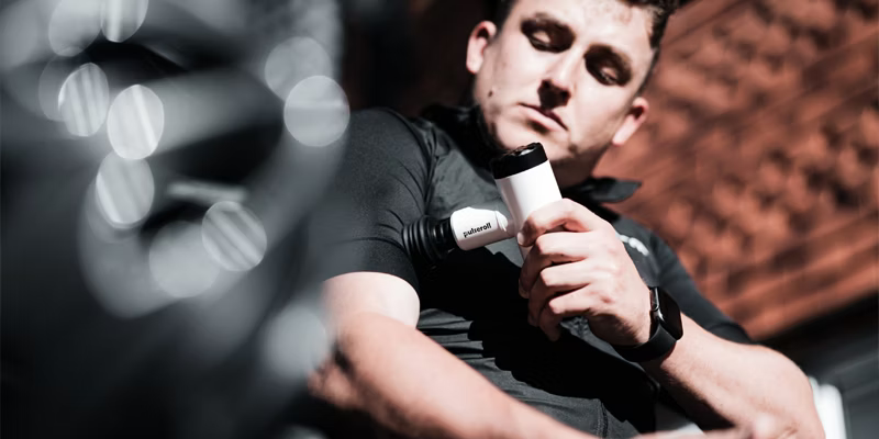 Man holding a Pulsar massage gun, resting after a workout.