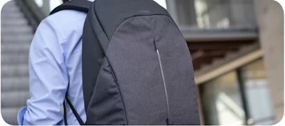 A person wearing a sleek, black backpack while standing outdoors near modern architecture.