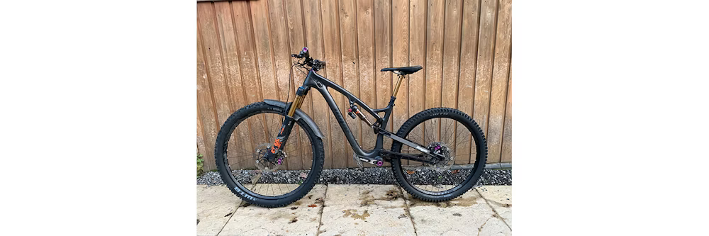 A black mountain bike with a sleek design, parked in front of a wooden fence on a stone patio.