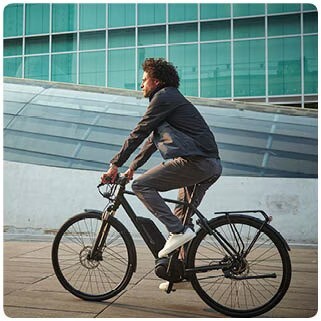 Man commuting on a black bicycle in an urban area, wearing casual clothing and cycling past modern architecture.