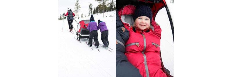 Family skiing while pulling a child in a red trailer through the snow; a close-up of a smiling child bundled in warm clothes inside the trailer.