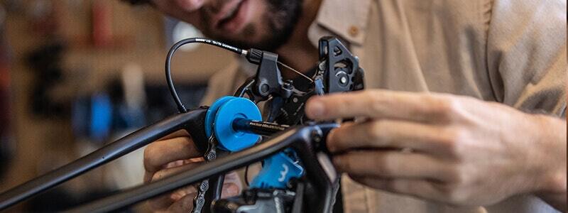 A man performing maintenance on a bike, focusing on the rear derailleur using a blue ChainGrip tool.