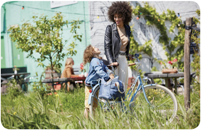 Mother and daughter smiling beside a blue bicycle in a grassy garden