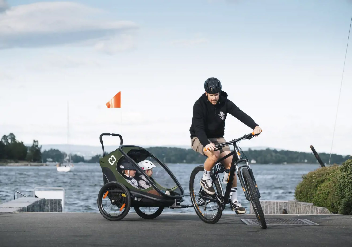 Hamax Outback 2-seat bike trailer hitched to bicycle carrying two children