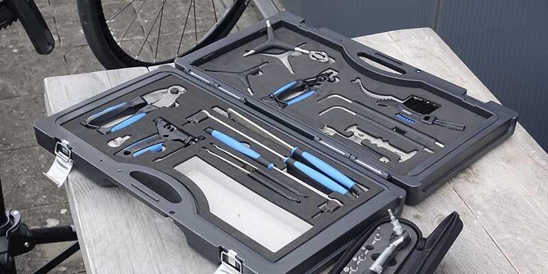 Open bike repair toolkit with various tools organized in a case, placed on a wooden table.