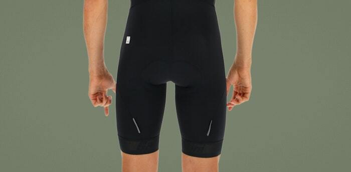 Rear view of a cyclist wearing black bib shorts with reflective details, standing against a green background