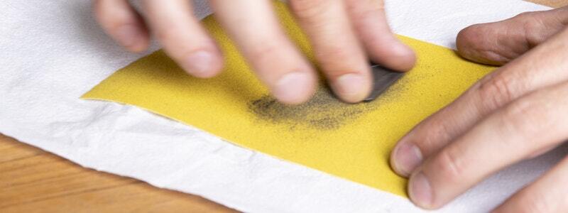 Sanding a brake pad on yellow sandpaper to remove residue