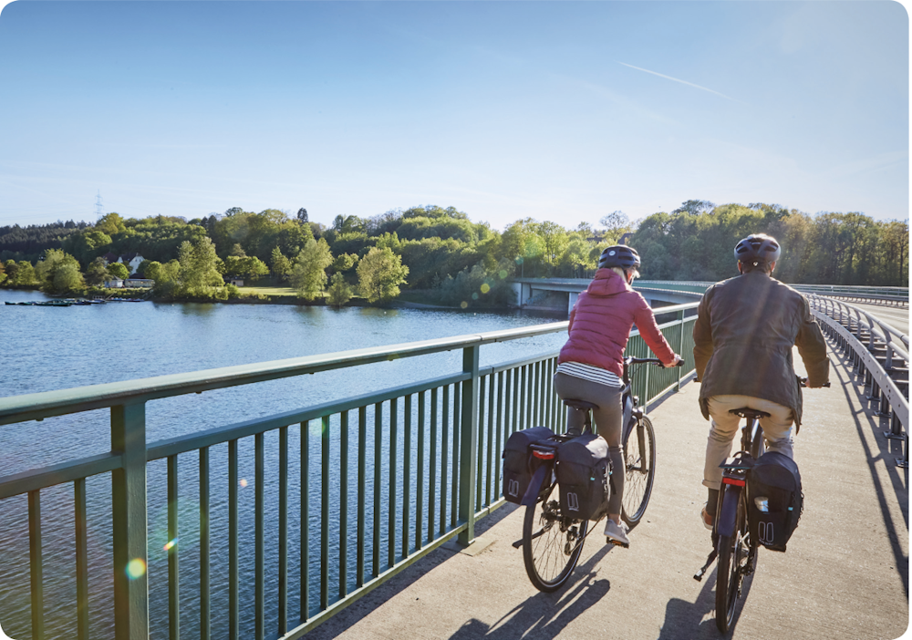 Two cyclists riding across a bridge over a scenic lake