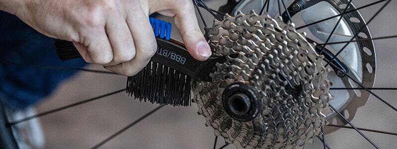 Person cleaning a bicycle cassette with a toothbrush-style cleaning tool.