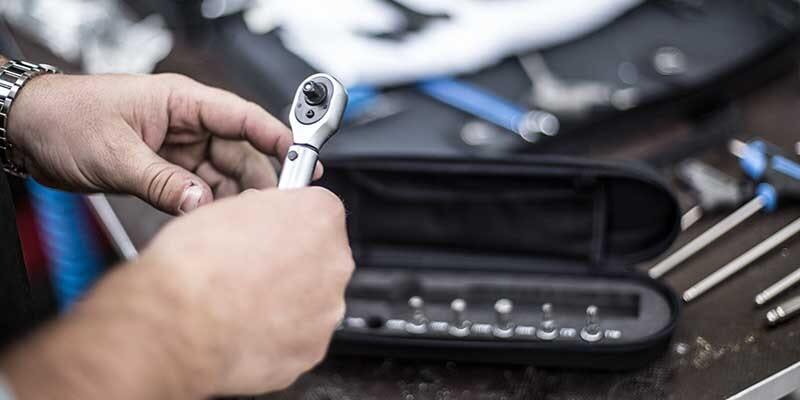 Close-up of hands holding a torque wrench, with a toolset and other repair tools in the background.