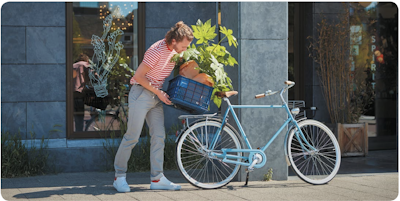 Woman unloading groceries and a plant from a blue commuter bicycle