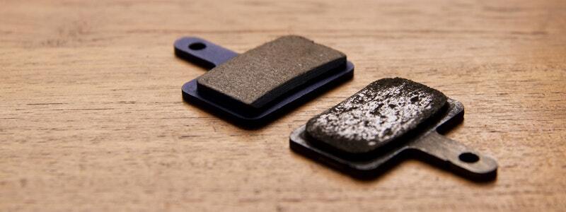 Worn vs. new brake pads displayed on a wooden surface