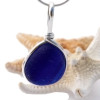 A thick blue sea glass pendant in our Original Wire Bezel setting.
This is a really neat piece of sea glass from the UK that seems almost dark blue. Yet a thin line of lighter blue runs through the bottom side. Left TOTALLY UNALTERED from the way it was collected on Seaham Beach in England.