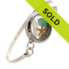 Flashed green genuine sea glass from England is combined with a fresh water stick pearl and real starfish in this stainless steel locket and presented on a solid sterling bangle bracelet