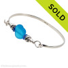 Two pieces of beach found sea glass in bright  blue on this solid sterling silver sea glass bangle bracelet. The center bead is handmade by a glass artist and resembles vivid electric aqua sea glass. Finished with sea life beads that have images of dolphins frolicking around.
Sorry this sea glass jewelry piece has been sold!