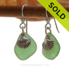 A simple pair of genuine green sea glass earrings with sterling shell charms in a lightweight simple setting.