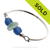 A thick piece of very round piece of sea green English Seaham Sea Glass combined with two bright blue recycled glass beads on a solid sterling bangle bracelet.