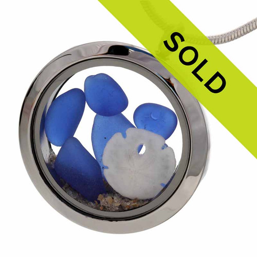 Blue sea glass pieces combined with a real sandollar and beach sand in this sea glass locket necklace.