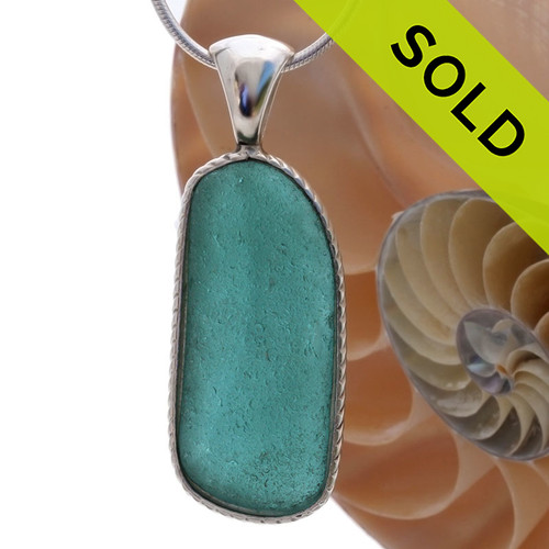 A really neat almost perfectly flat but long and thick piece of VIVID Teal green sea glass set in our Deluxe Wire Bezel© necklace pendant setting.
Sorry this piece of sea glass jewelry has been sold!
