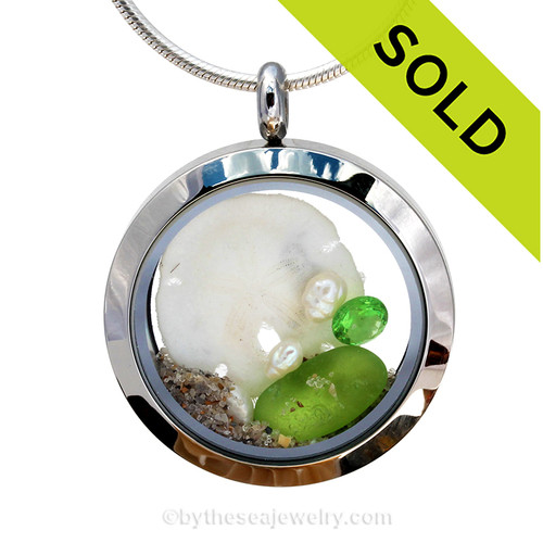 Genuine lime green sea glass piece combined with a real sandollar, fresh water pearls and real beach sand in this stainless steel locket.
Finished with a  vivid peridot crystal gems for a bit of beachy bling.