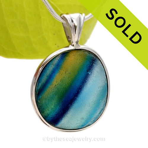 A True SUPER ULTRA ULTRA RARE Genuine Seaham Sea Glass Multi set in our Deluxe Wire Bezel© Pendant Setting.

These colors are totally natural to this type of sea glass as they were accidentally fused together over 100 years ago then tossed into the North Sea as waste. Two color sea glass pieces from this region are more common, these amazing 4+ pieces are highly prized around the world today. This piece is LARGE (SEE product details below) and not available through any other sea glass artist in the world today! Shades of Blue, Aqua, Green  Purple and Yellow are streaked inside this amazing sea glass piece.
SOLD - Sorry this Ultra Rare Sea Glass Pendant is NO LONGER AVAILABLE!