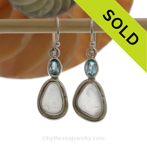 A stunning pair of pure white sea glass earrings set in a finely crafted setting in sterling silver finished with a beach bling brilliant Blue Topaz round gem.