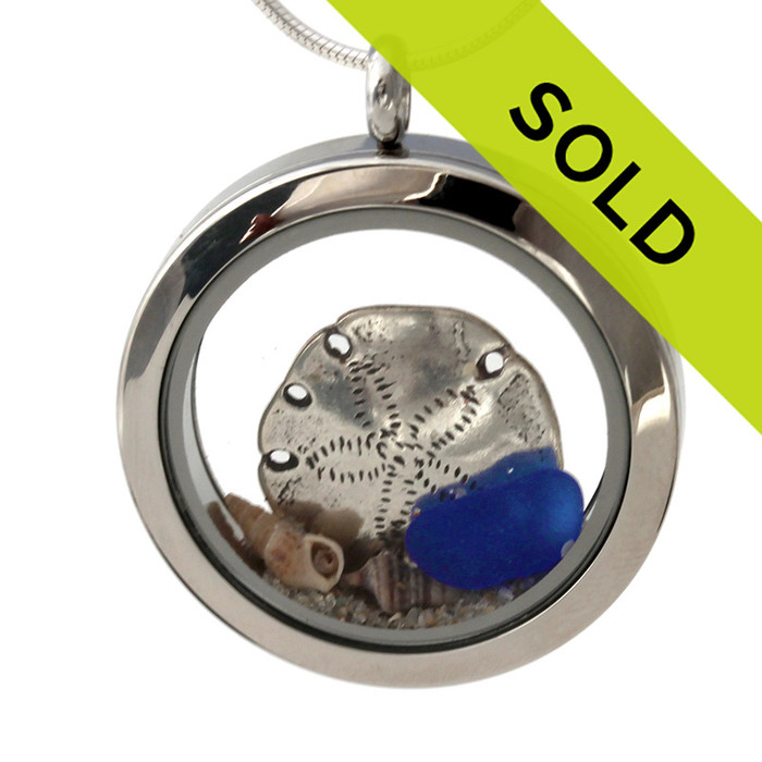 Simple small blue sea glass combined with a  sterling silver sandollar and small beach shells in this beach on the go stainless steel locket necklace.