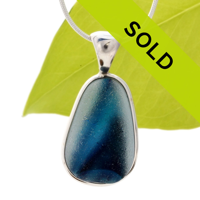 A vivid blue in a clear base. This piece was once the tip of a punty or pontil rod used to gather and work glass in the kiln. The color being worked was the rich brown at the bottom.
Sorry this one of a kind sea glass jewelry piece has been sold!