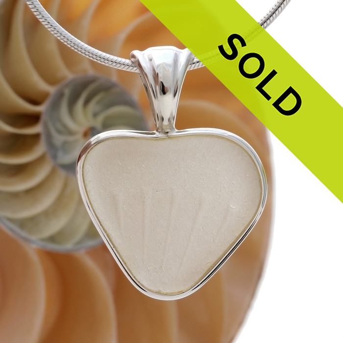 A beautiful white natural sea glass heart set in our deluxe wire bezel setting.
Genuine sea glass hearts are a RARE phenomena and cherished among sea glass lovers!
This one is unique as it has distinct embossing that radiates from the point.