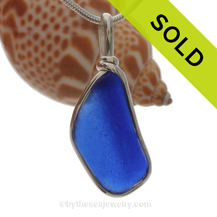 A lovely piece of Cobalt Blue Sea Glass from a bottle or jar bottom set that is set in our Original Deluxe Wire Bezel© necklace pendant in Solid Sterling Silver. 

This original By The Sea Jewelry setting that encases the glass in silver and leaves both front and back open so you can feel the texture of this antique top quality glass.