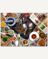  A stone cutting board covered with a variety of colorful spices, surrounded by small bowls, an open cookbook, and a mortar and pestle. 