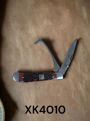 Twisted X brown hoof pick and serrated folding knife combo tool for horse care and ranch use displayed on tan background