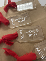 Want, need, wear, and read gift tags with red ribbons on kraft paper