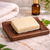 Dark wooden rectangular soap dish with drainage slots holding a natural soap bar on a bathroom countertop