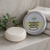 Avocado Oil and Shea Butter conditioner bar by The Ginger Goats shown beside its tin packaging on a wet bathroom ledge with folded towels, highlighting a natural, deeply nourishing solid conditioner for soft, healthy hair.
