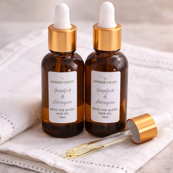 Two amber glass dropper bottles of Grapefruit and Lemongrass Hair Oil from The Ginger Goats, placed on a soft fabric surface with a glass pipette, styled in a clean, fresh and minimal setting.
