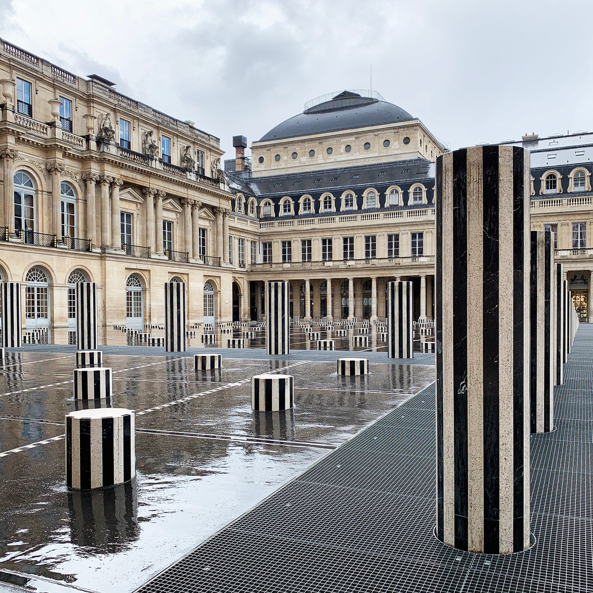 Palais Royal after the rain. The black-and-white columns of Daniel Buren reflect across the wet courtyard, creating one of the most photographed and recognizable scenes in Paris.