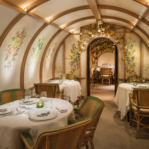 Beneath graceful wooden arches, Arpège reveals one of Paris's most intimate dining rooms. Botanical artwork, woven chairs and soft lighting echo Alain Passard's celebrated devotion to vegetables, flowers and the changing seasons, creating a setting that feels quietly refined rather than theatrical.