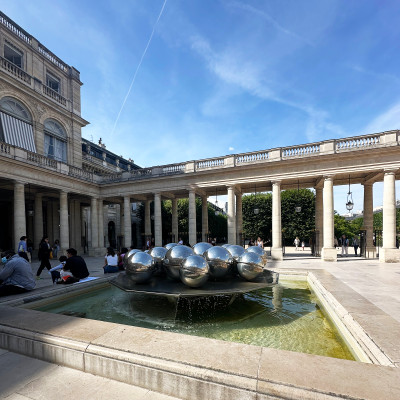Visitors explore the Cour d'Honneur beneath dramatic Paris skies. Surrounded by elegant arcades and historic architecture, Palais Royal blends contemporary art with classical design.