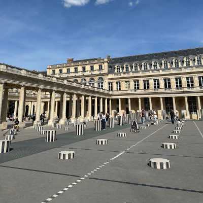 Visitors explore the Cour d'Honneur beneath Paris blue skies. Surrounded by elegant arcades and historic architecture, Palais Royal blends contemporary art with classical design.