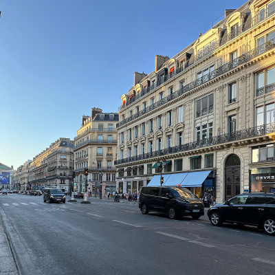 A simple, everyday view of Avenue de l'Opéra—wide sidewalks, classic Haussmann façades, steady traffic, and a natural flow of Parisians and visitors moving between the Opéra and the Louvre, with cafés and boutiques lining the street.