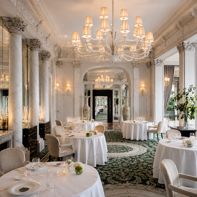 An elegant dining experience at Le Pré Catelan, nestled within the lush greenery of the Bois de Boulogne. The image captures the refined ambiance of the restaurant’s grand dining room—ornate chandeliers, crisp white linens, and impeccably plated dishes that reflect the artistry of three Michelin star French cuisine. A timeless setting where culinary excellence meets Parisian sophistication. Captured for TLC Paris.