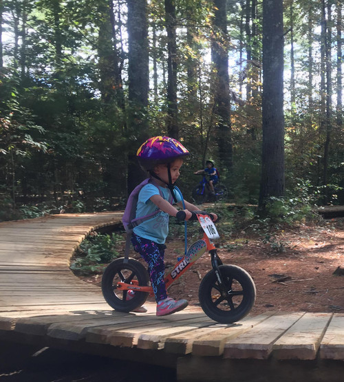 A girl striding on her Strider 12 Sport balance bike while at an outdoor bike park