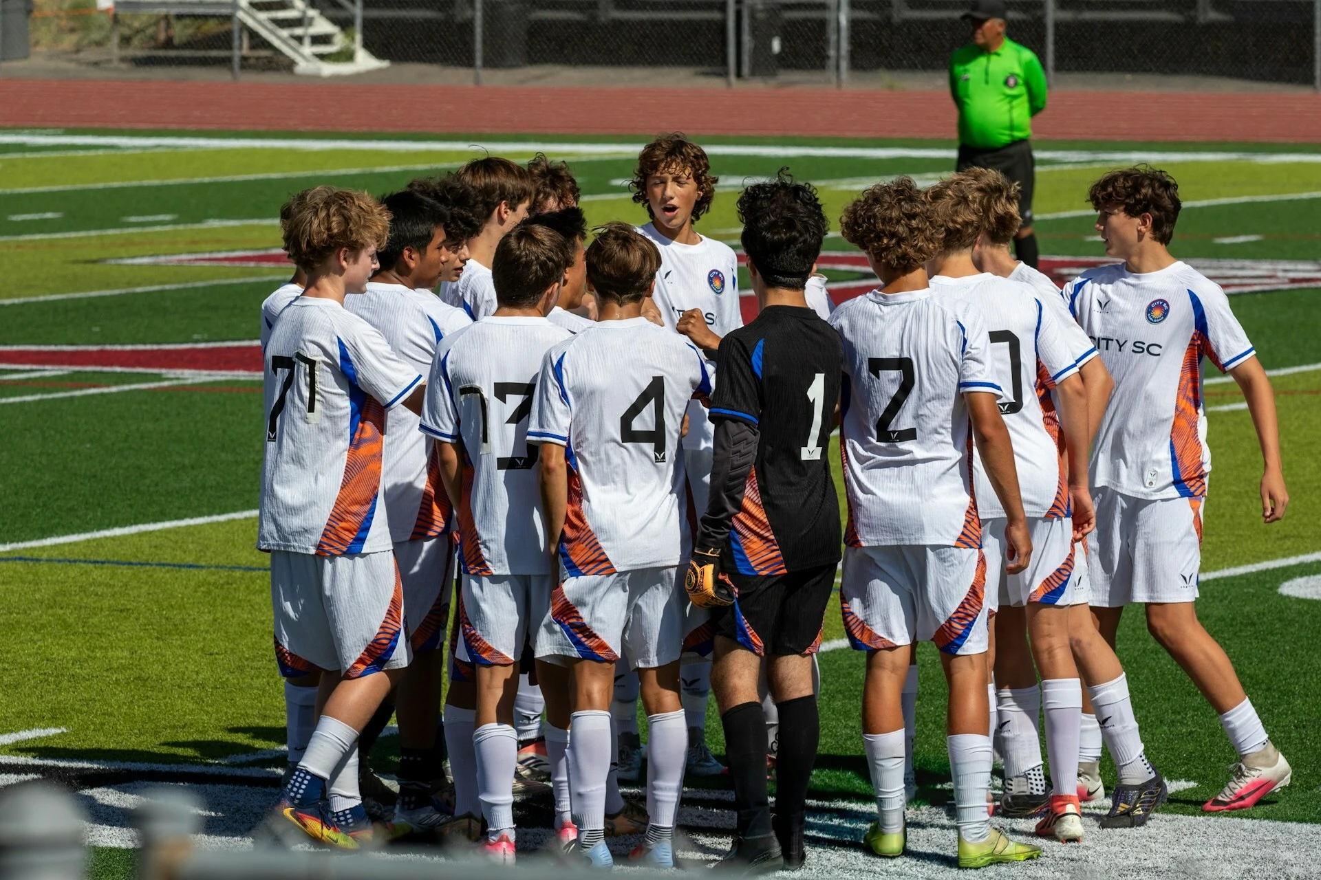 Youth soccer players huddle with their coach on the field before a game