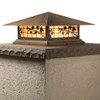 A classic, traditional sloped-roof column mounted pier light fixture with crown molding accent, an aged bronze finish, floral artwork and golden glass. 