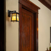 A classic Arts & Crafts style fixed arm wall sconce light fixture with an aged bronze finish and warm glass installed on an interior wall of a Craftsman style home.