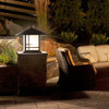 A linear, formal Craftsman column mounted pier lantern with bronze finish and warm white glass installed on a back patio seating area with a fire pit and different seating options. This Arts & Crafts fixture has a Japanese-inspired screen pattern on the body. 